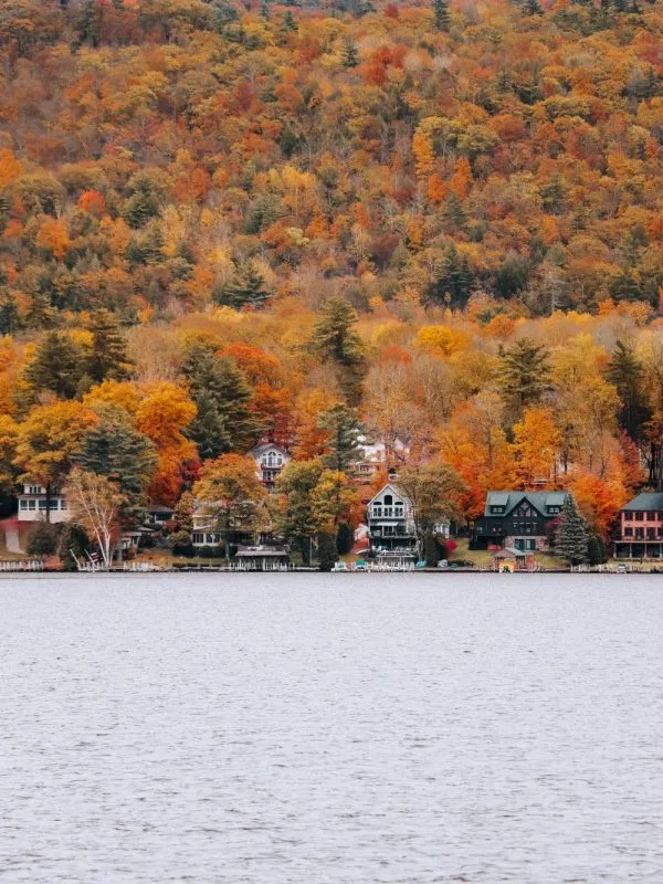 Colorful autumn foliage in New York State reflected above lakeside houses, a peaceful fall landscape perfect for scenic family travel in the USA.