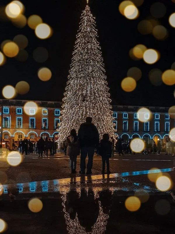 Family standing in front of a giant illuminated Christmas tree in Lisbon at night, reflecting on the wet pavement during a magical winter family travel moment in Portugal.