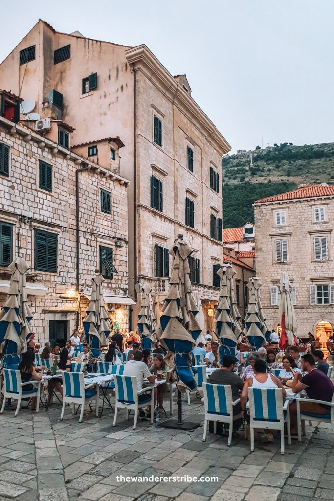People enjoying an evening meal at a charming open-air restaurant in a cobbled square of Dubrovnik’s Old Town during a Croatia road trip.