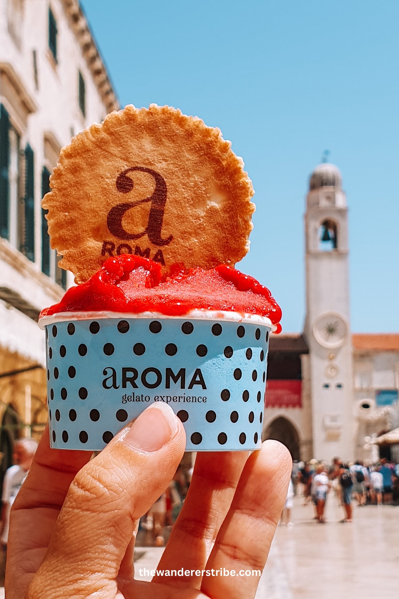 Close-up of strawberry gelato from Aroma Gelato on a sunny day in Dubrovnik Old Town, Croatia, with the clock tower in the background.