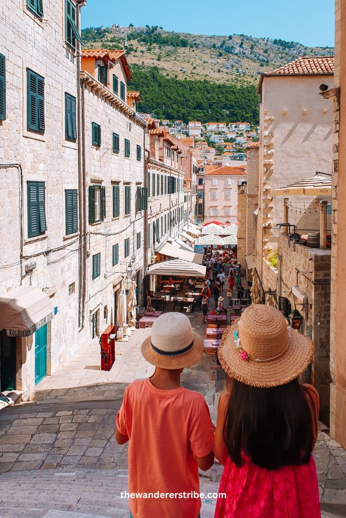Children in straw hats walking down the Jesuit Stairs in Dubrovnik Old Town, exploring the historic city with their family
