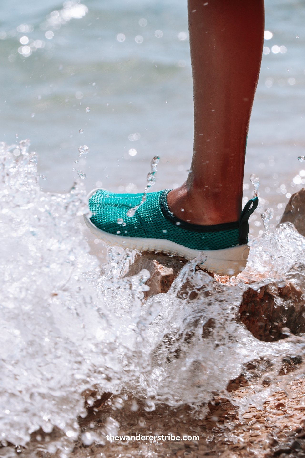 Close-up of a child’s foot wearing turquoise water shoes as waves splash against the rocks on a Dubrovnik beach.