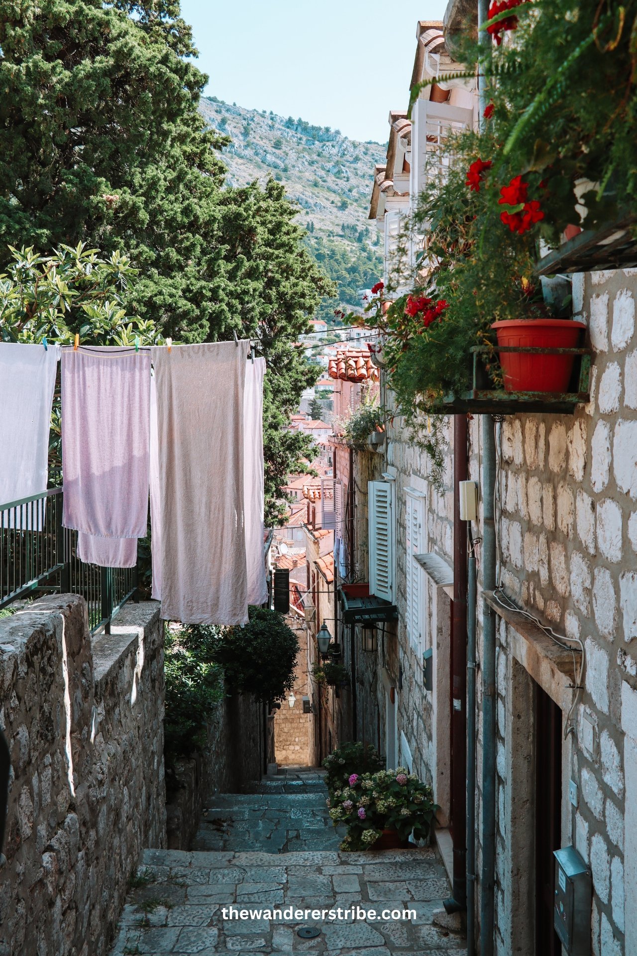 Laundry hanging to dry on a line in a quiet stone alley of Dubrovnik with a view of rooftops and hills.