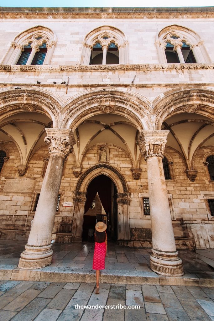 Young girl wearing a hat and summer dress entering the historic Rector's Palace in Dubrovnik during a family trip