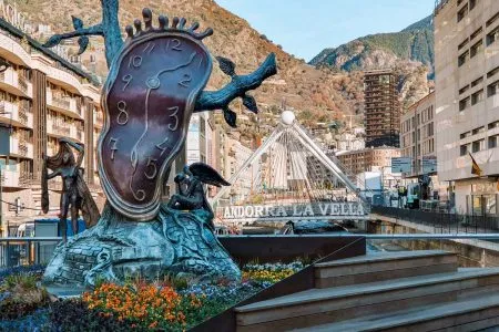 Salvador Dalí's Noblesa del Temps sculpture with its melting clock at Plaça de la Rotonda in Andorra la Vella, with the Gran Valira river, the "Andorra la Vella" bridge and mountains behind